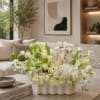White and green floral arrangement in a low white vase on a coffee table