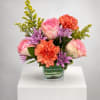 Pink roses, orange carnations, and purple daisies in a glass vase
