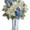 White lilies and blue flowers arranged in a silver vase with a cross