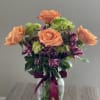 Peach roses and purple flowers in a glass vase with a ribbon