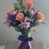 Bouquet of peach roses and purple flowers in a glass vase with a purple ribbon