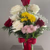Mixed bouquet of roses, daisies, and pink flowers in a glass vase with a red bow