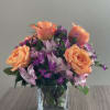 Peach roses and purple flowers in a clear glass vase