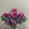 Pink roses and purple flowers arranged in a clear glass vase.