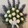 White roses and purple filler flowers in a white vase with a ribbon.