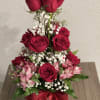 Tiered bouquet of red roses and pink flowers in a glass vase with a red ribbon