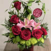 Red roses and pink lilies arranged in a red vase with a heart sign
