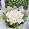Bouquet of cream-colored roses wrapped in patterned white and kraft paper with a bow.