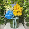 Tall glass vase with yellow roses, blue hydrangea, white orchids and an 'It’s a Boy' pick.
