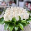 Low arrangement of cream roses tightly packed in a round glass vase with a collar of glossy green leaves.