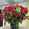 Large arrangement of red roses with abundant greenery in a clear glass cube vase tied with a black ribbon.
