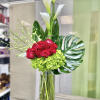 Tall arrangement of white calla lilies, red roses, and green hydrangeas in a clear glass cylinder vase