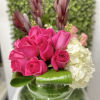 Low glass vase with hot pink roses, white hydrangea, and looped green leaves in a compact arrangement