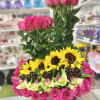 Structured arrangement of hot pink roses, yellow sunflowers, green orchids and grapes in a low glass vase