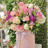 Round pink hatbox filled with pink, white, and purple mixed roses and carnations.