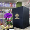 Single purple rose under a glass dome with a black gift box beside it