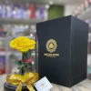 Single yellow rose under a glass dome with gold ribbon on black base beside a tall black gift box