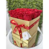 Square gold box filled with tightly packed red roses and tied with a red ribbon.