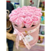 Round pink box filled with tightly packed light pink roses and tied with a printed ribbon.