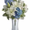 White lilies and blue flowers arranged in a silver vase with a cross