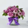 Pink roses and daisy-like flowers in a glass vase with a purple ribbon