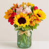 Bouquet of sunflowers, lilies, and carnations in a green glass jar