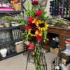 Tall floral cross with red roses, sunflowers, and orange lilies