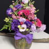 Colorful bouquet of pink and purple flowers in a textured glass vase with a purple ribbon