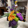 Colorful bouquet in a glass vase with orange gerberas, green mums, and purple carnations