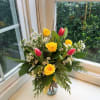 Yellow roses and pink tulips in a glass vase with white filler flowers
