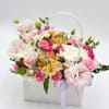 Pastel flower arrangement in a white handled box with a lavender ribbon
