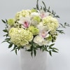 White and pale green floral arrangement in a white vase with pink orchid accents