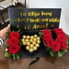 Red roses and gold-wrapped chocolates in a black gift box with a love message