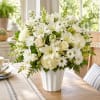 White floral arrangement in a white vase with lilies, roses, and daisies