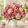 Pink lilies and mixed blooms arranged in a white vase