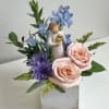 Pink roses and purple flowers in a square vase with a small angel figurine