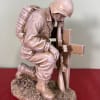 Stone soldier kneeling beside a cross memorial statue