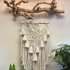 Macrame wall hanging suspended from a driftwood branch with potted plants below