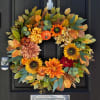 Autumn wreath with sunflowers, dahlias, and small pumpkins in orange and yellow tones on a dark door