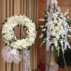 Two white funeral flower wreaths with condolence ribbons on stands