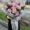 Handheld bouquet of pink roses wrapped in gray paper with ribbon