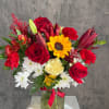 Mixed bouquet of red roses, lilies, sunflowers, and white daisies in a glass vase