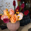 Peach roses and magenta flowers arranged in a pink vase