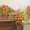 Sympathy set with orange roses and yellow sunflowers on a casket, in a vase, and on a standing spray.