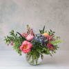 Colorful arrangement of pink peonies, hydrangea, and mixed blooms in a round glass vase