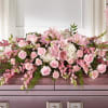 Pink and white floral arrangement with roses and lilies on a casket