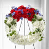 Heart-shaped floral wreath with red roses, white chrysanthemums, and blue flowers on a stand