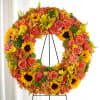 Large floral wreath with sunflowers, roses, and orange blooms on a black stand