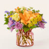 Orange lilies and mixed flowers in a pink glass vase