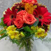Bouquet of red gerbera daisies, coral roses, and yellow alstroemeria in a glass vase